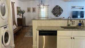 Una cucina compatta con lavastoviglie, forno a microonde e lavello. Il pavimento è in legno e al centro c'è un tappeto.