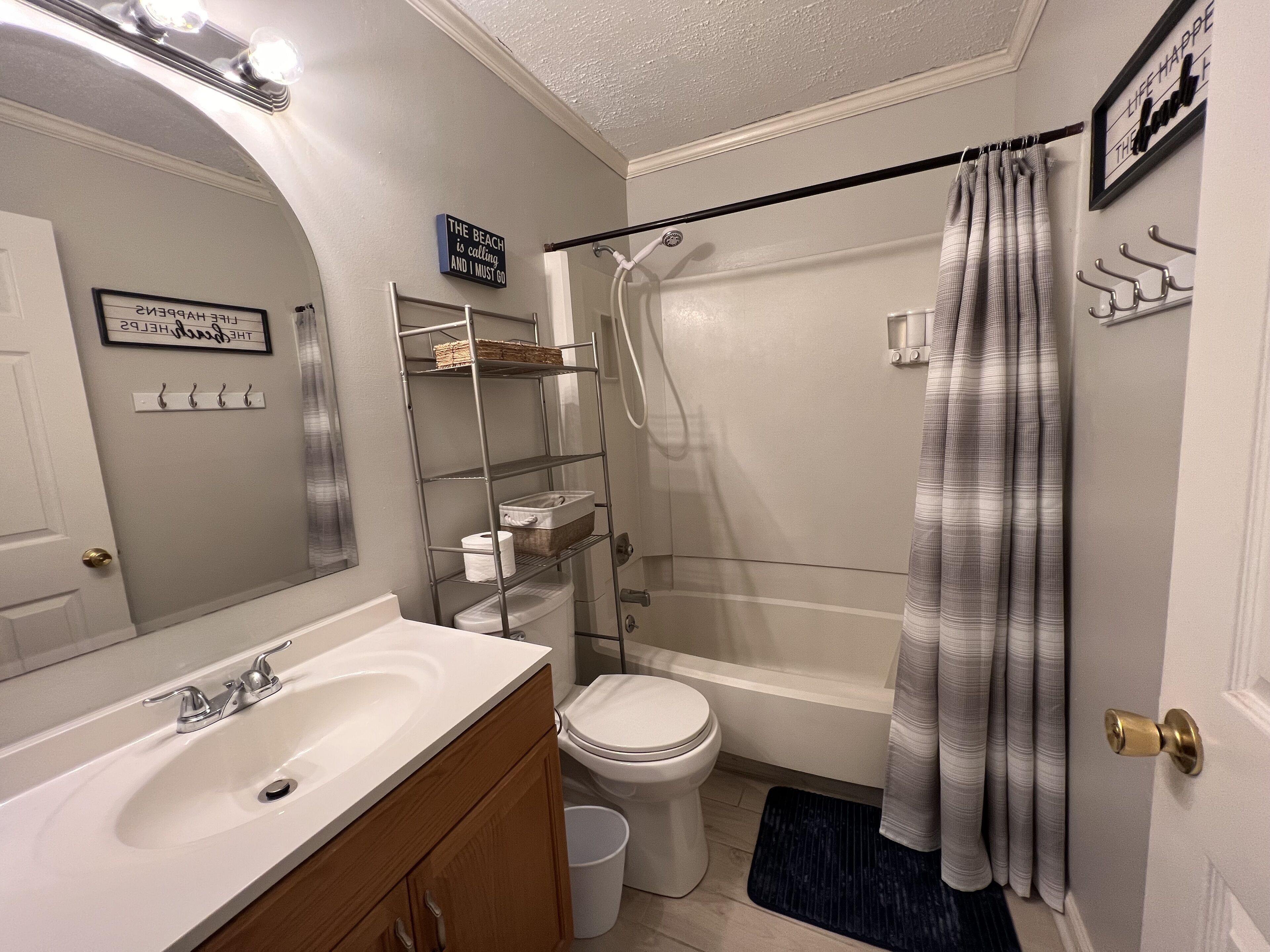 A bathroom with a white sink, toilet, and shower curtain. There is a shelf with toiletries and a towel rack.