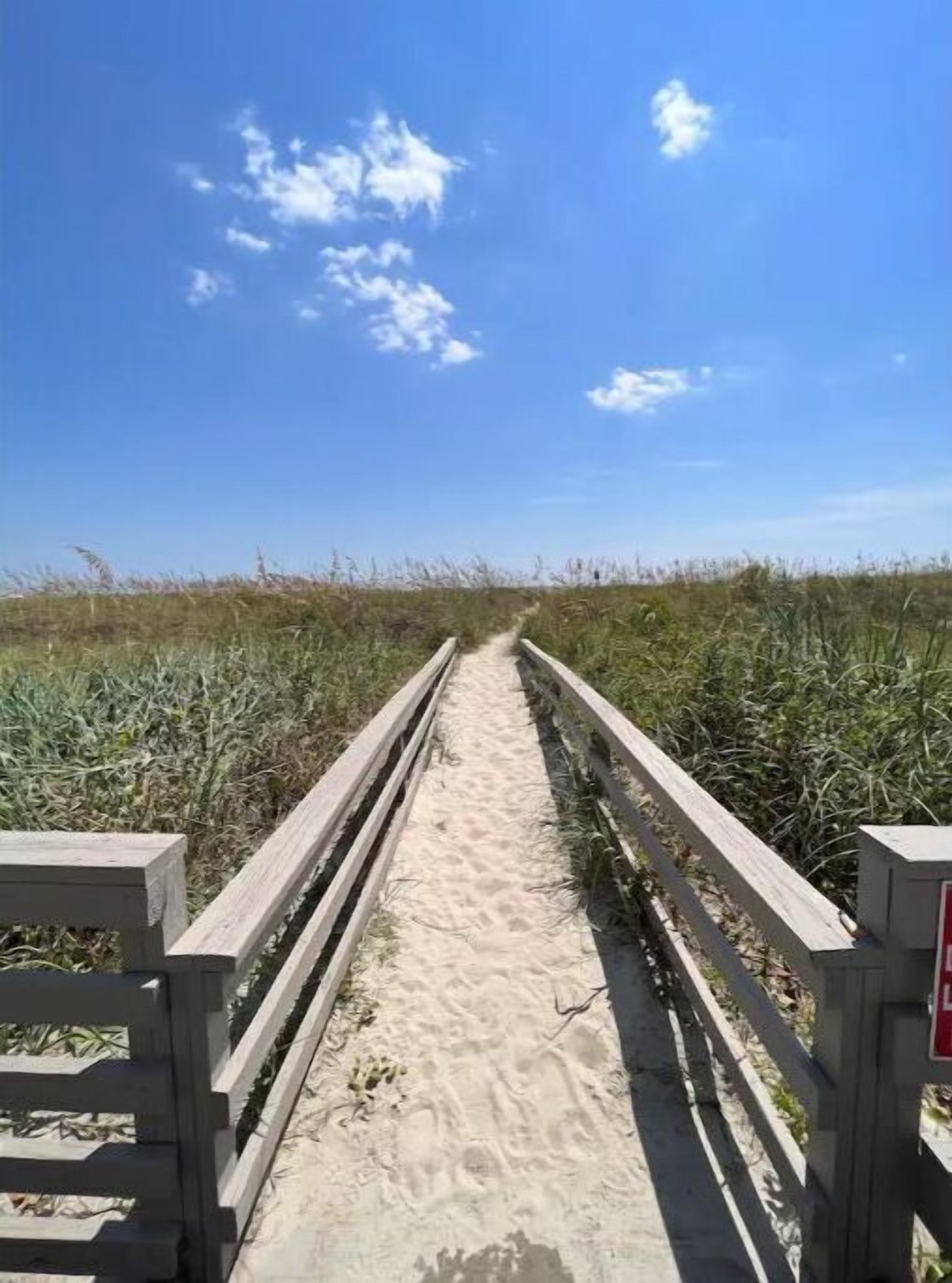 Un sentier sablonneux menant à une plage, avec des garde-corps en bois de chaque côté.