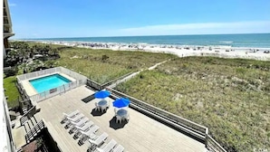 A pool area with lounge chairs and umbrellas, overlooking a beach with a clear sky. - Tequila Sunrise - 2BR Oceanfront (North Myrtle Beach)