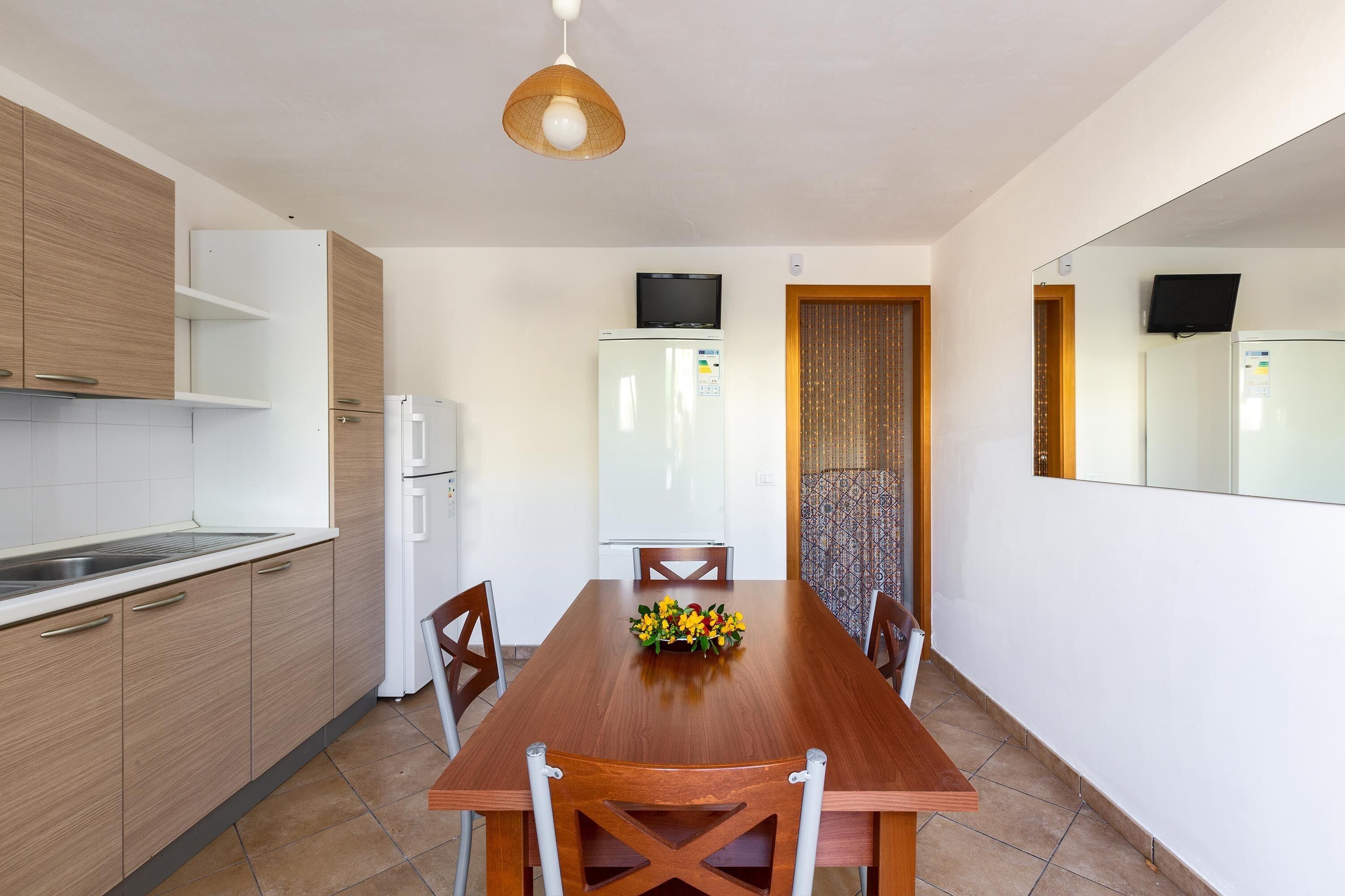 A modern kitchen with wooden cabinets, a white refrigerator, and a dining table with chairs.