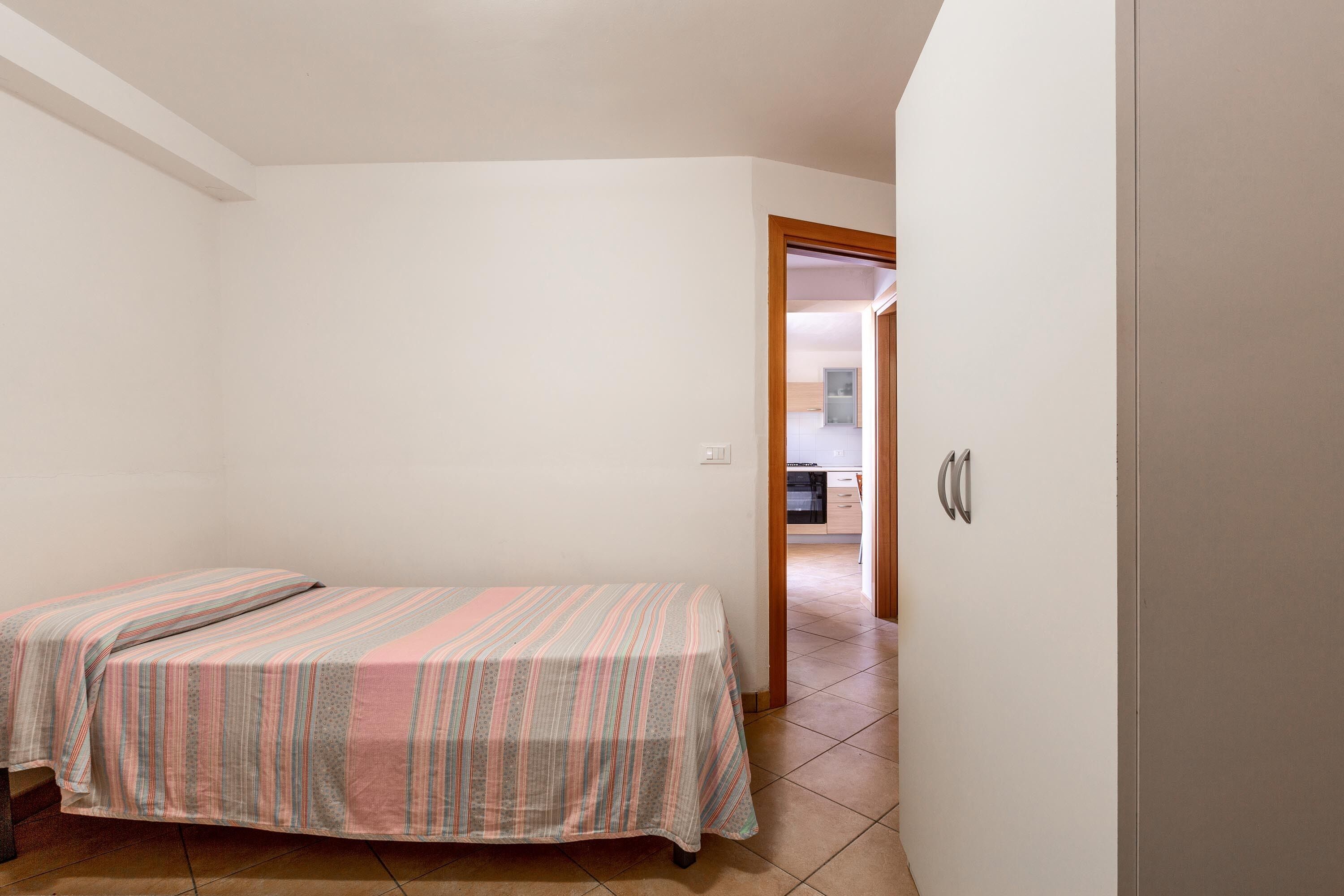 A small, single-bed room with a striped bedspread, white walls, and a tiled floor.