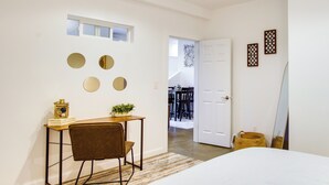 A bedroom with a bed, a desk with a chair, a small table with a plant, and a mirror. There is a door leading to a dining area. - Chic & Modern Snohomish Hideaway on a Working Farm (Snohomish)