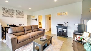 A modern living room with a brown leather sofa, a coffee table, and a dining area with a table and chairs. There is a kitchen area with a refrigerator and a microwave. - Chic & Modern Snohomish Hideaway on a Working Farm (Snohomish)