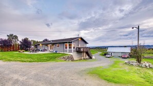A two-story building with a porch and a small deck, surrounded by a gravel driveway and grassy areas. - Chic & Modern Snohomish Hideaway on a Working Farm (Snohomish)