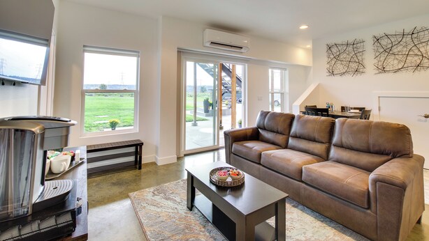 A modern living room with a leather sofa, a coffee table, and a fireplace. There are large windows offering a view of the outdoors. - Chic & Modern Snohomish Hideaway on a Working Farm (Snohomish)