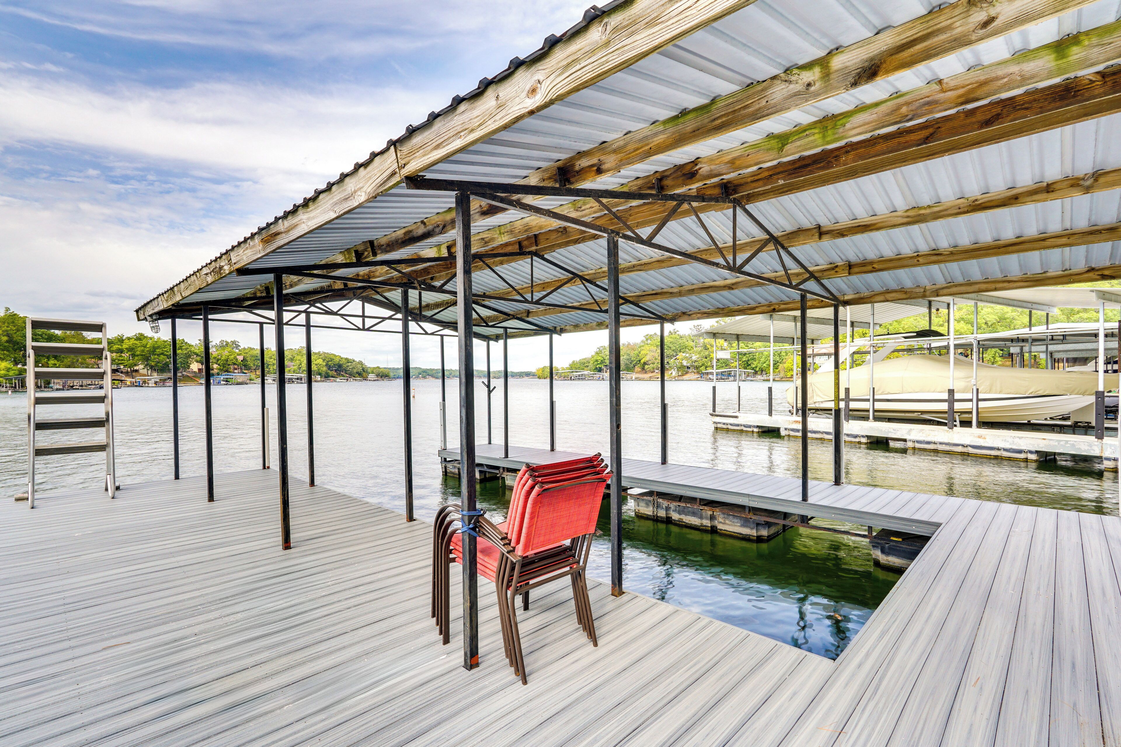 A covered dock with a chair, wooden deck, and a view of the water.