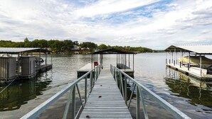 A wooden pier leading to a dock with covered seating areas and a boat. - Lakefront Home w/ Private Dock in Sunrise Beach! (Sunrise Beach)