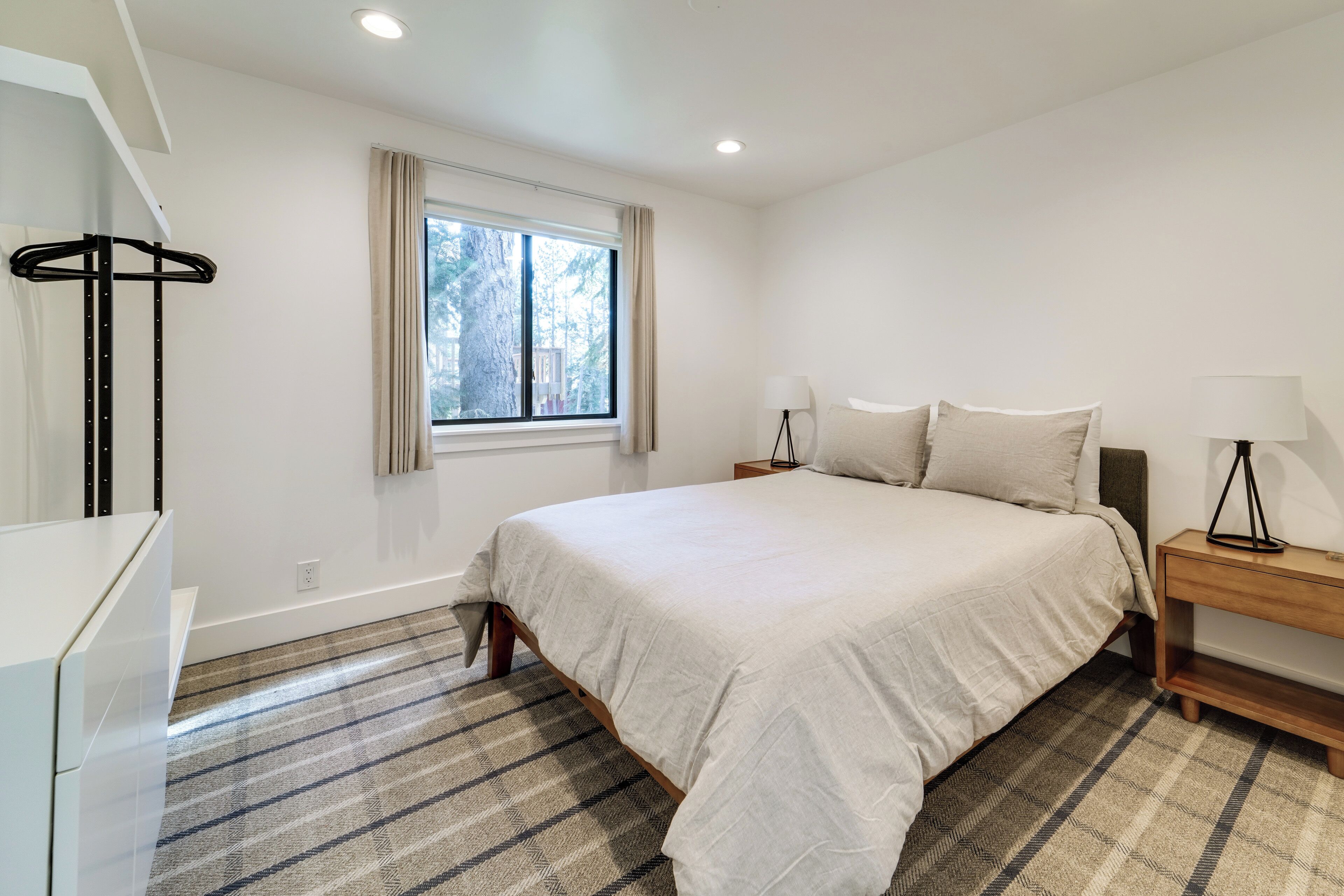 A bedroom with a bed, bedside tables, a lamp, a window with curtains, and a hanging light fixture.
