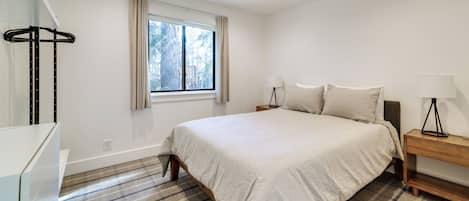 A bedroom with a bed, bedside tables, a lamp, a window with curtains, and a hanging light fixture.