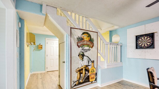 Une pièce avec un escalier, un jeu de fléchettes et une affiche de Jimmy Buffett.