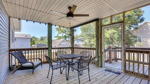 Une terrasse extérieure couverte, équipée d’une table et de chaises, d’un ventilateur de plafond et offrant une vue sur les maisons voisines.