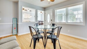 Un coin repas avec une table en verre entourée de chaises, un ventilateur de plafond et une pancarte indiquant « BIENVENUE ».