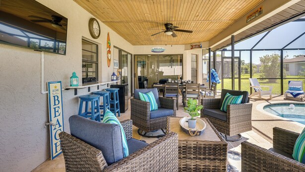 A covered outdoor seating area with wicker furniture, a pool, and a bar.