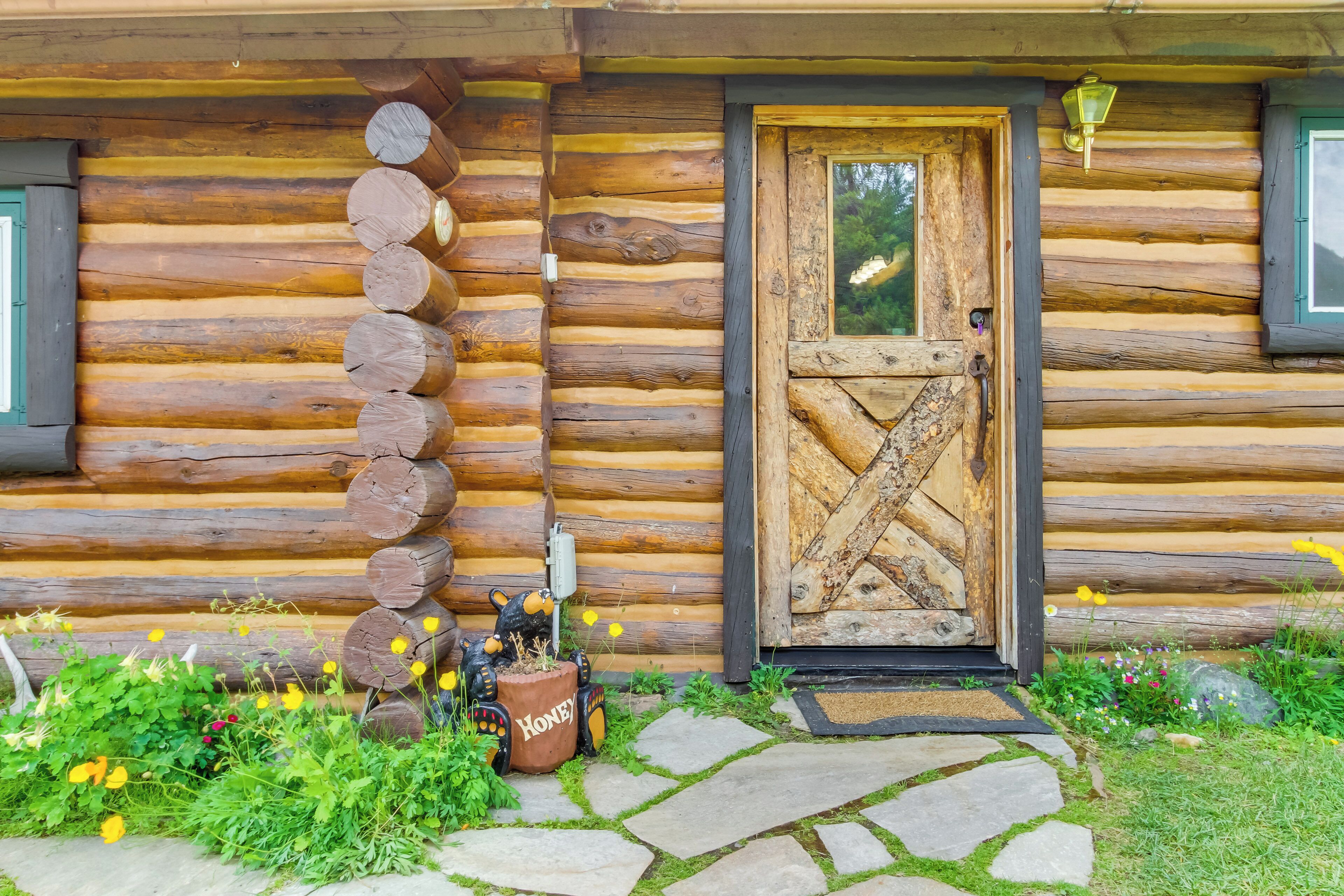Una cabaña de troncos con una puerta de madera, un camino de piedra y una decoración con bote de miel.