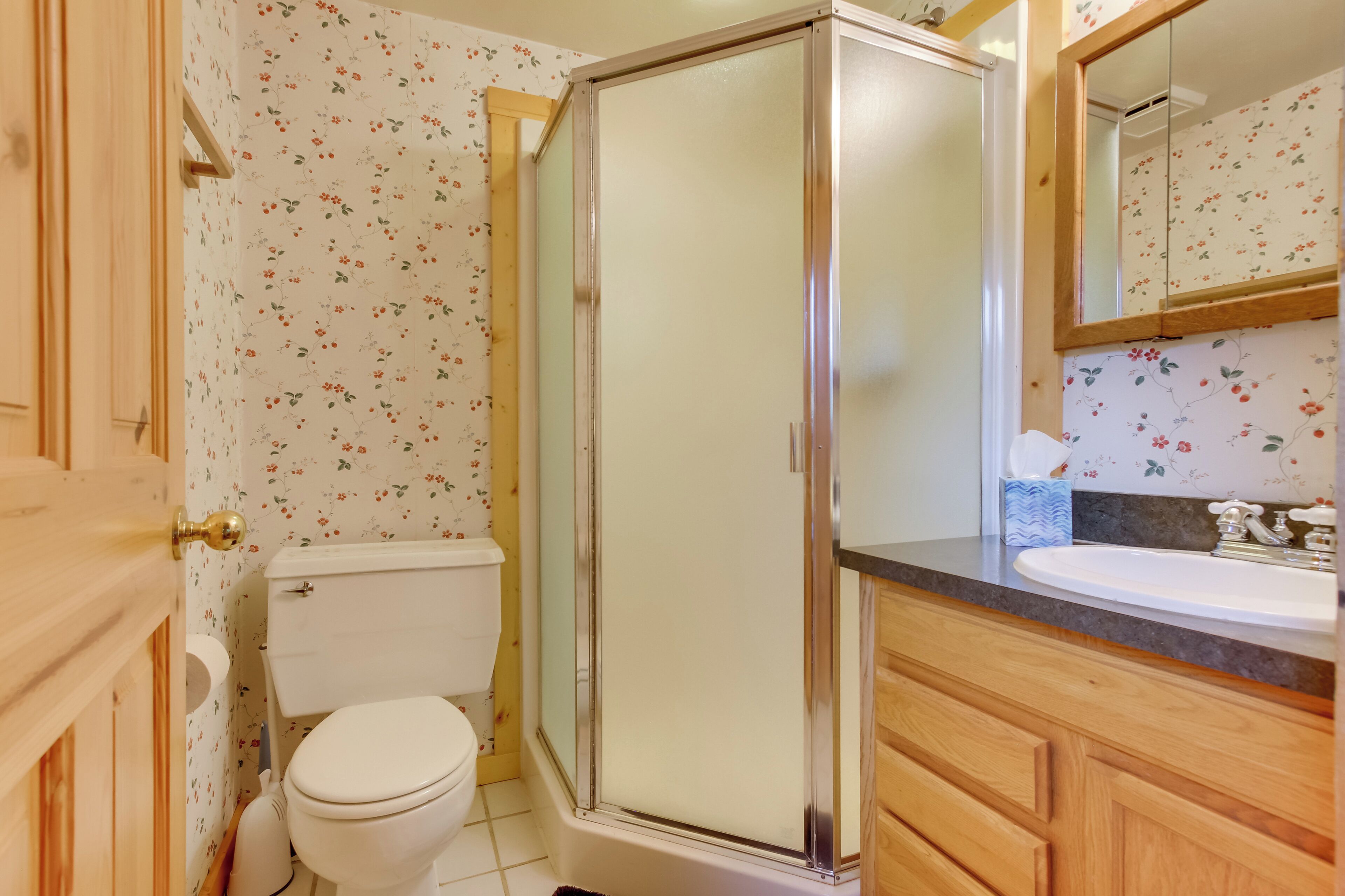 Een badkamer met toilet, douchecabine, wastafel en houten kastjes.