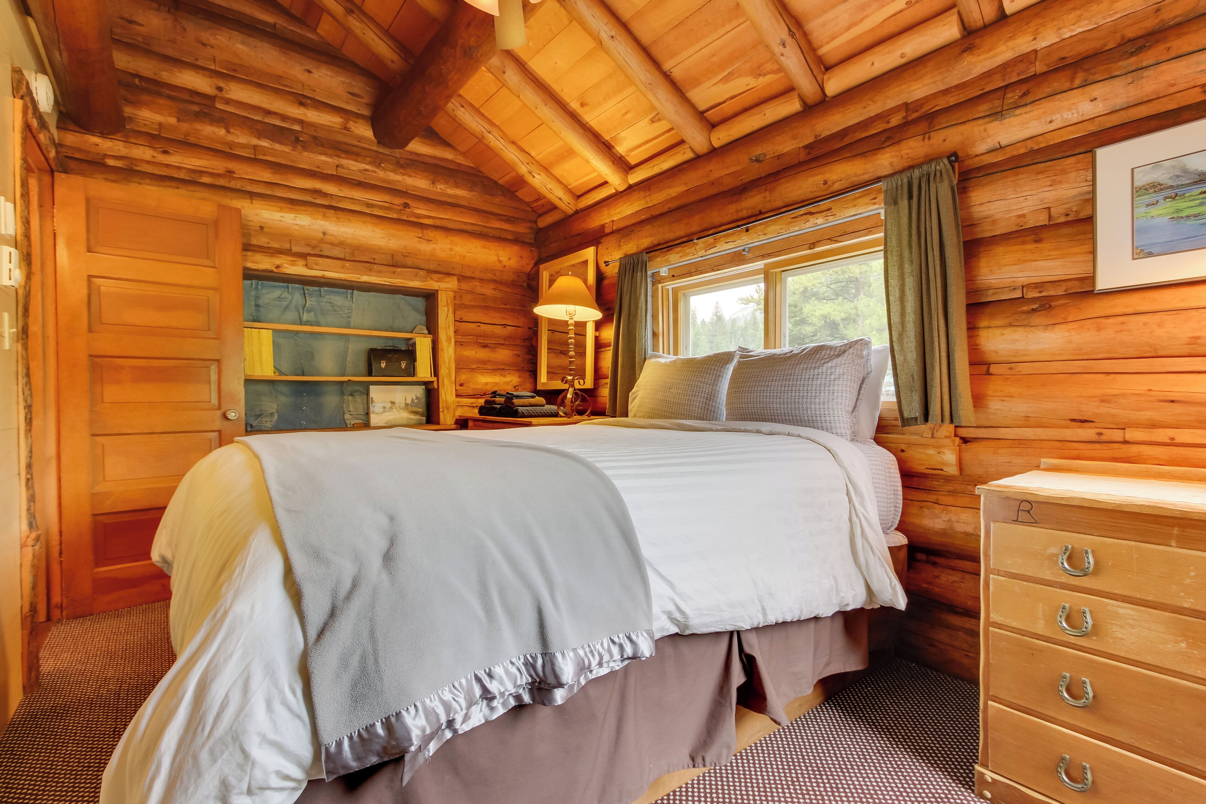 A cozy wooden cabin bedroom with a bed, dresser, and a window with curtains.