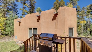 A wooden deck with a barbecue grill, a wooden railing, and a building with a stucco exterior and two windows with shutters. - Secluded Amalia Retreat w/ Cozy Fireplace & Grill! (Amalia)