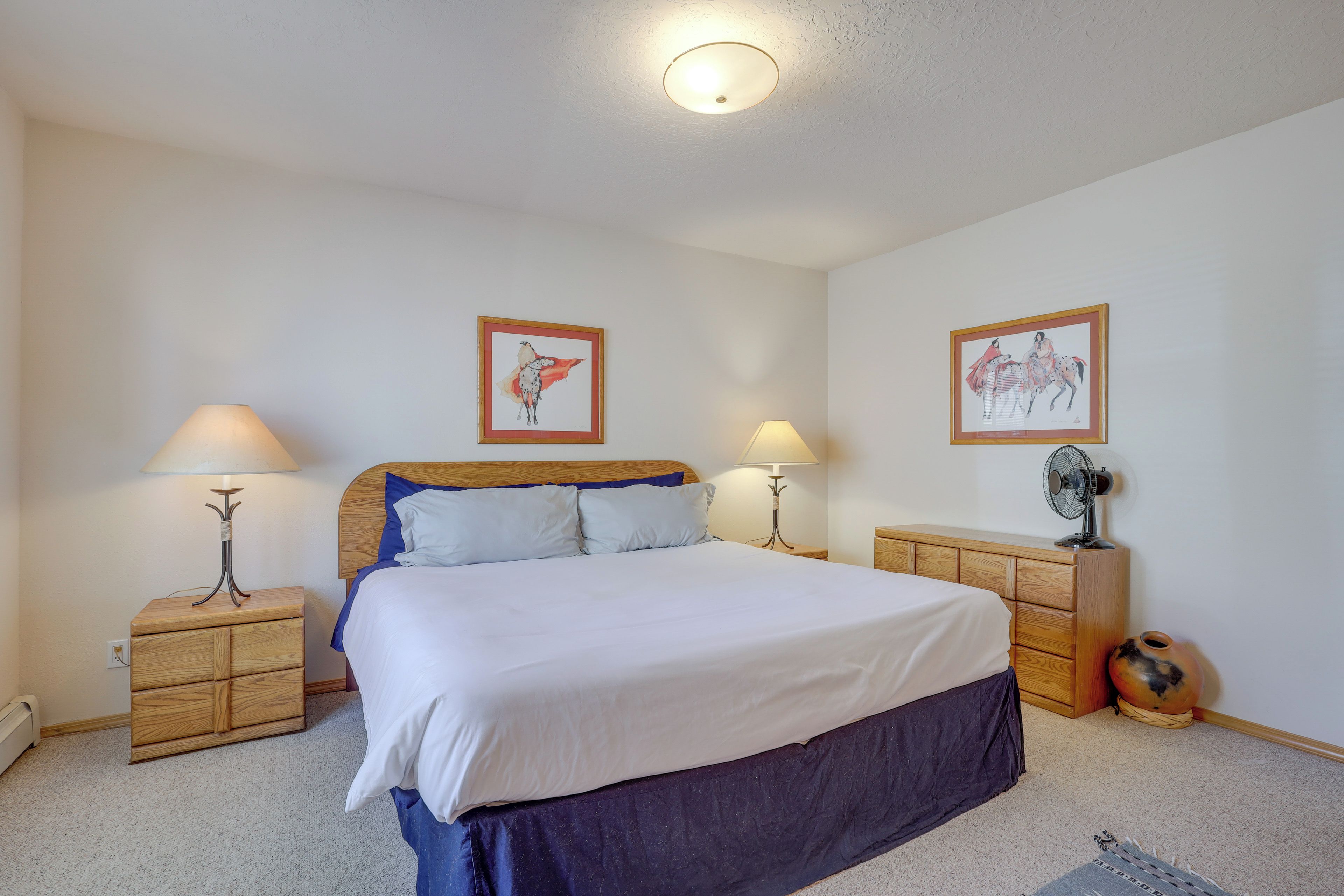 A bedroom with a bed, two nightstands, a dresser, and two wall-mounted lamps.