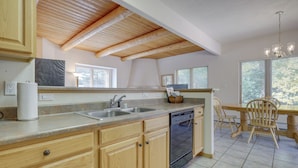 A kitchen with wooden cabinets, a dishwasher, a sink, and a dining area with chairs. - Secluded Amalia Retreat w/ Cozy Fireplace & Grill! (Amalia)