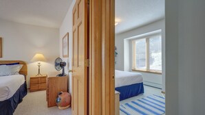 A bedroom with two beds, a wooden wardrobe, a bedside table with a lamp, a fan, and a window with blinds. - Secluded Amalia Retreat w/ Cozy Fireplace & Grill! (Amalia)