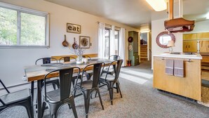 Ein Essbereich mit Holztisch und -stühlen, eine Küche mit Arbeitsplatte und Schränken sowie ein Fenster mit Jalousien.