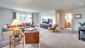 Ein geräumiges Wohnzimmer mit einer Couch, einem Couchtisch und einem Fernseher. Eine Tür führt in einen weiteren Raum.