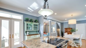 A kitchen with a granite countertop, stainless steel appliances, and a dining area with white furniture. - Waterfront Lusby Escape w/ Fire Pit & Kayaks! (Lusby)