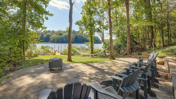 A patio with Adirondack chairs, a fire pit, and a hammock overlooking a lake. - Waterfront Lusby Escape w/ Fire Pit & Kayaks! (Lusby)