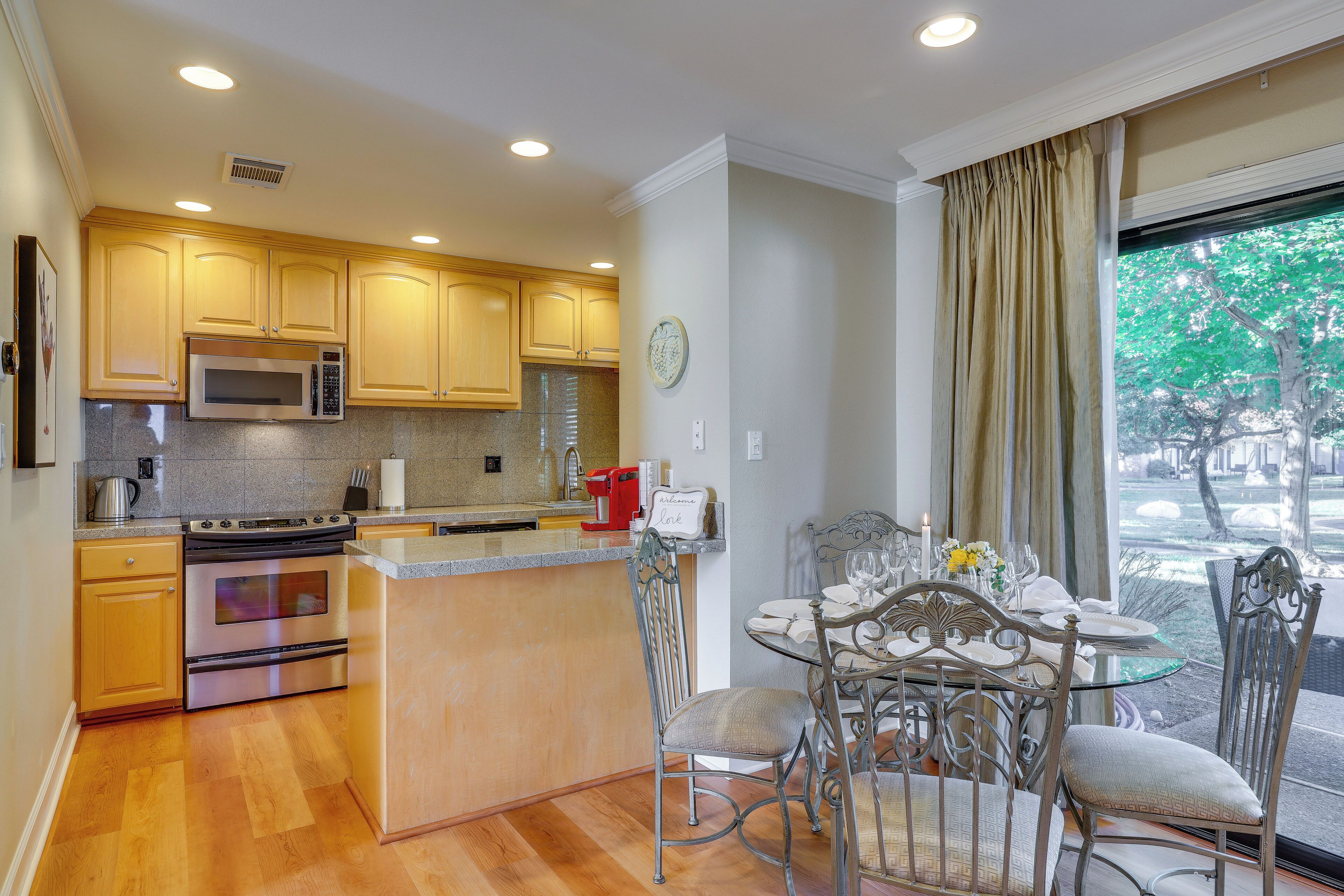 A kitchen with wooden cabinets, stainless steel appliances, and a dining area with metal chairs and a glass table.