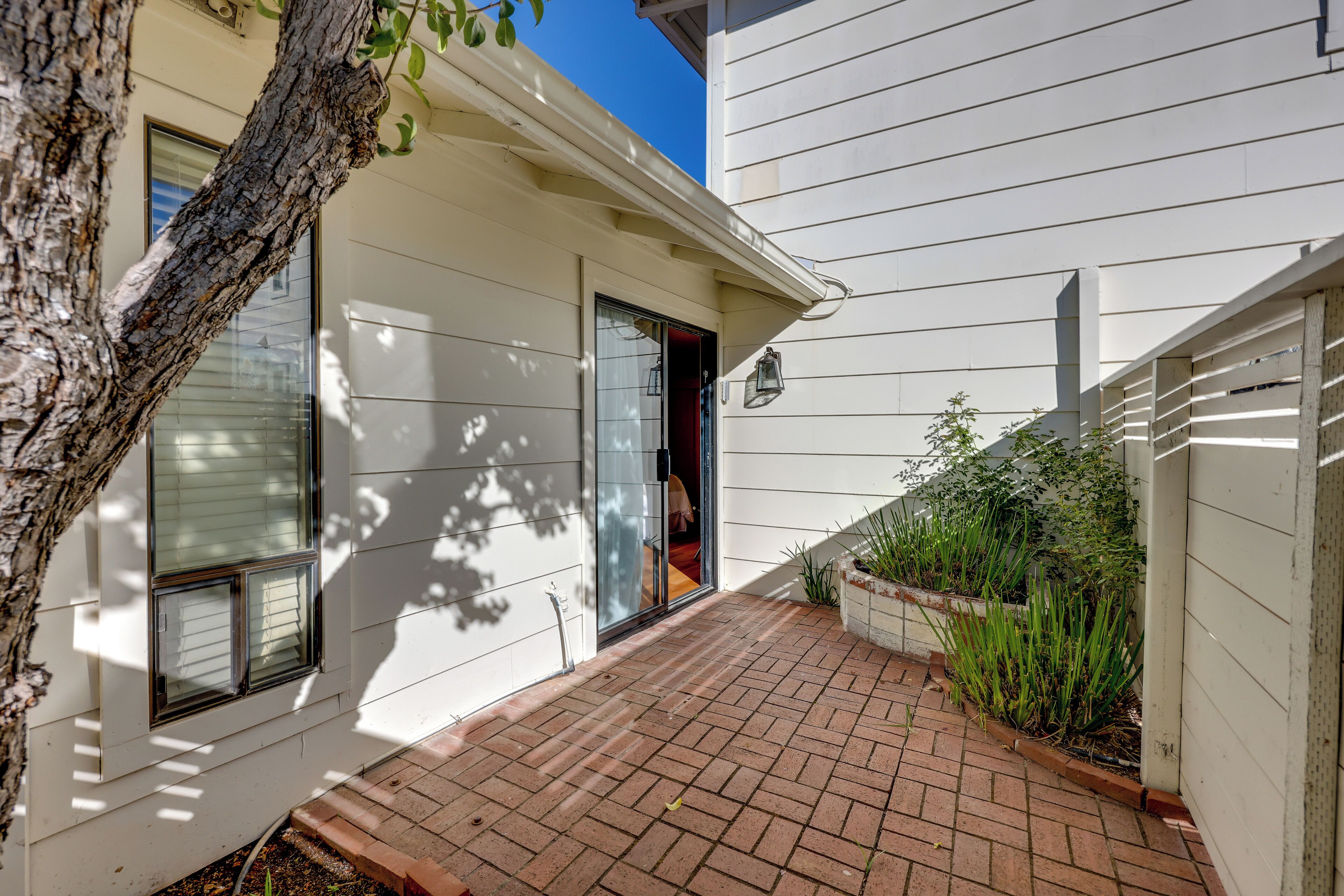 A house with a brick pathway leading to a glass door, surrounded by white siding and a tree.