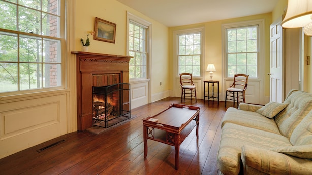 Une pièce avec une cheminée, un plancher en bois, un canapé et deux fauteuils.