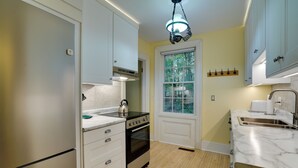 Une cuisine avec des meubles blancs, une cuisinière, un four, un évier et une fenêtre donnant sur des arbres.