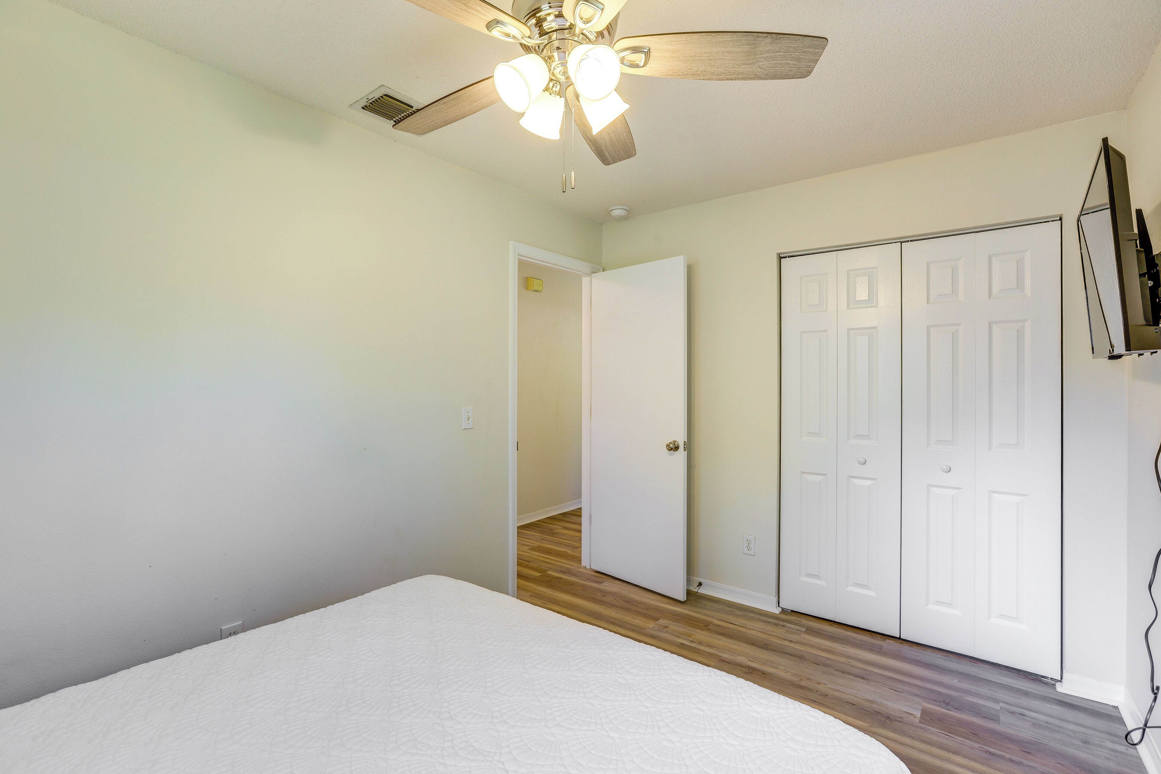 A bedroom with a bed, a ceiling fan, wooden flooring, and white doors.
