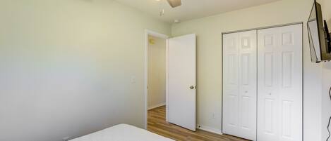 A bedroom with a bed, a ceiling fan, wooden flooring, and white doors.