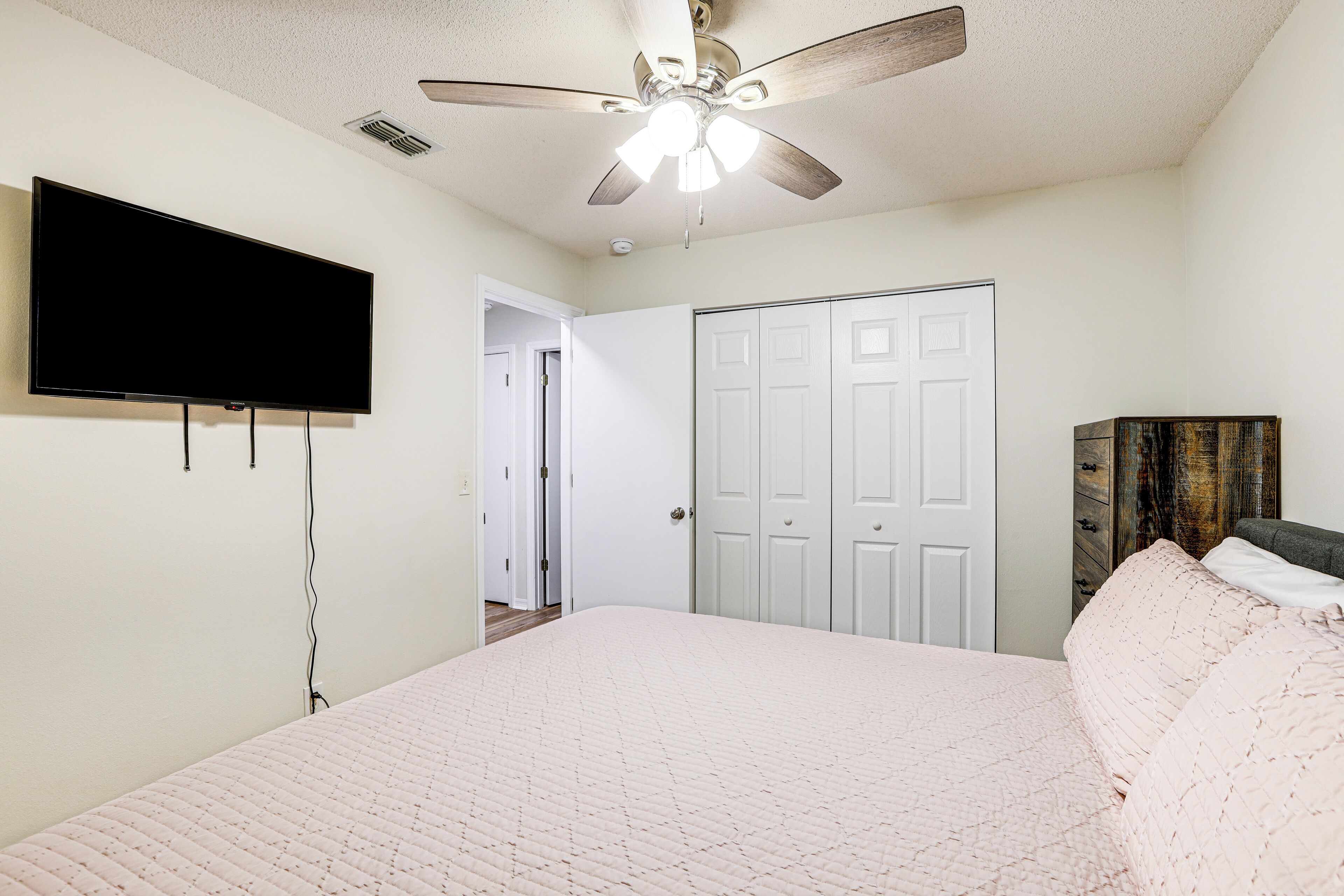 A bedroom with a bed, a ceiling fan, a TV mounted on the wall, and a wardrobe.