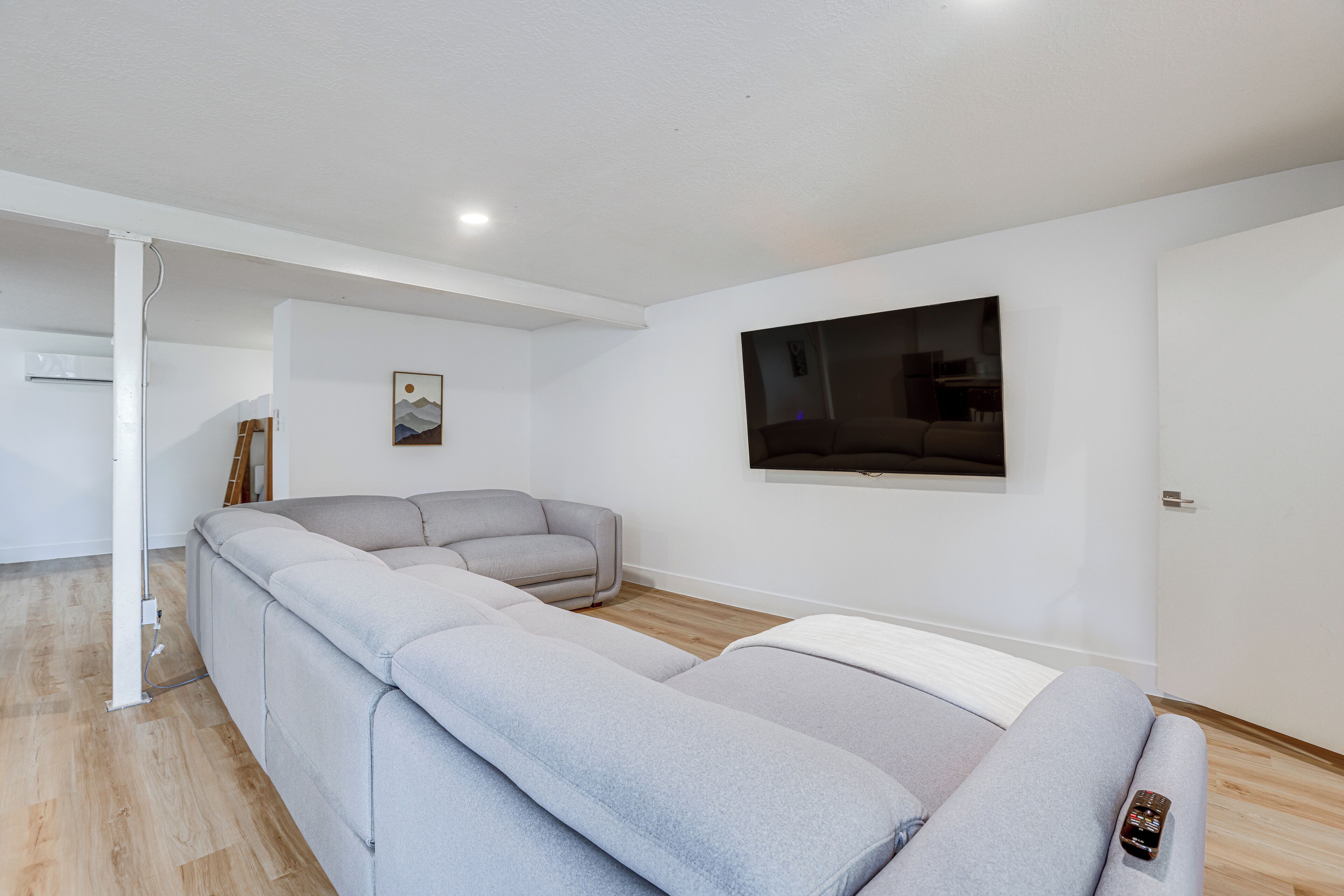 Ein modernes Wohnzimmer mit einem grauen Ecksofa, einem Flachbildfernseher an der Wand und Holzboden.