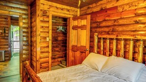 Un dormitorio de cabaña de madera con una cama, una puerta y un armario pequeño.