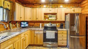 Una cocina tipo cabaña de madera con encimeras de granito, un refrigerador de acero inoxidable, una estufa y armarios de madera.