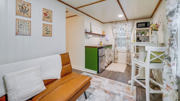 A cozy living room with a brown sofa, a green cabinet, and a kitchen area with a microwave and a small table. - Wilmington Area Studio ~ 4 Mi to Downtown! (Leland)