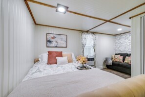 A bedroom with a bed, a sofa, a painting, and a window with curtains.
