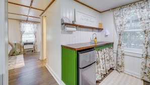 A compact kitchen with a green accent wall, a built-in refrigerator, and a window with floral curtains. - Wilmington Area Studio ~ 4 Mi to Downtown! (Leland)