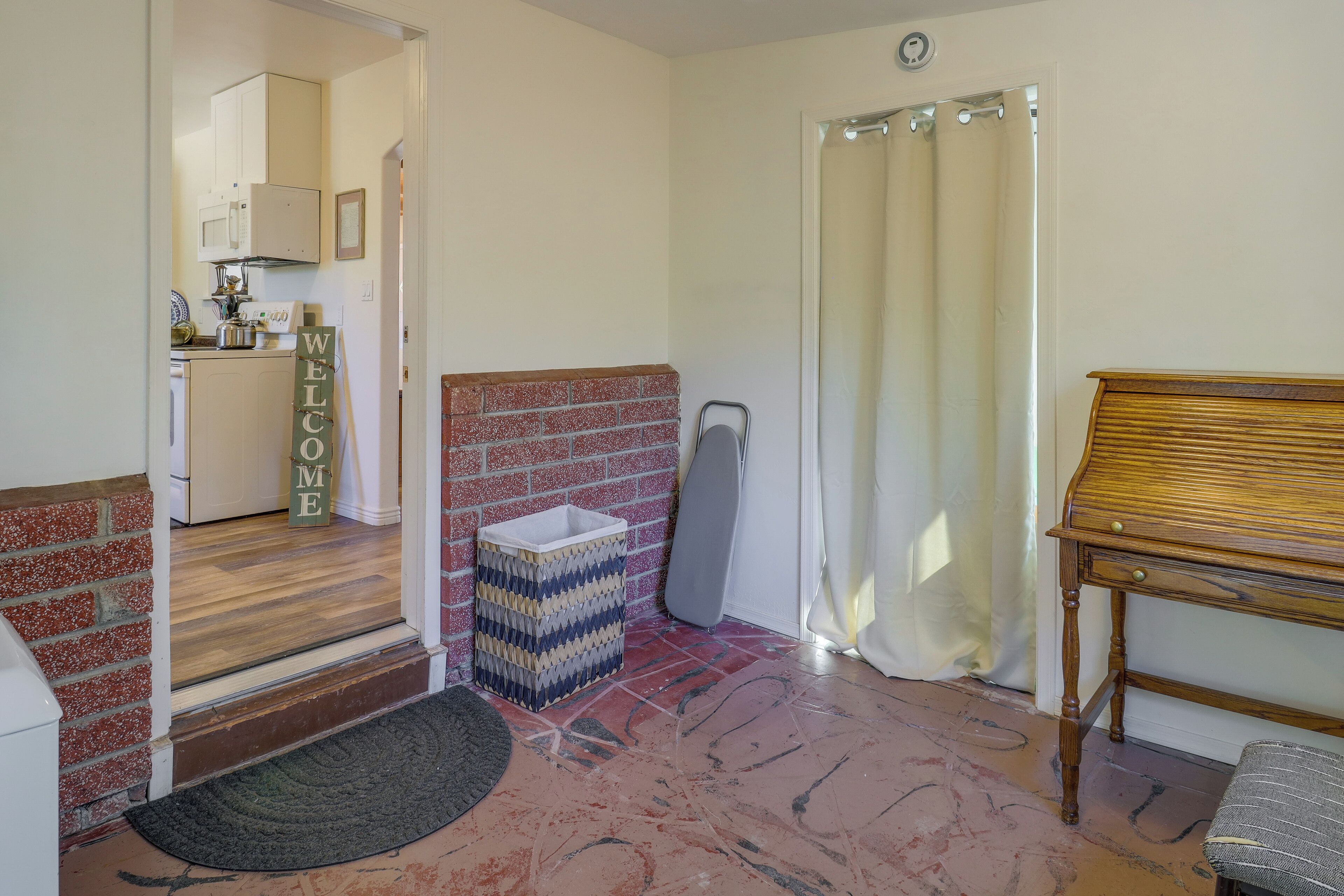 A room with a brick wall, a wooden bench, a welcome sign, a small trash bin, and a shower curtain.