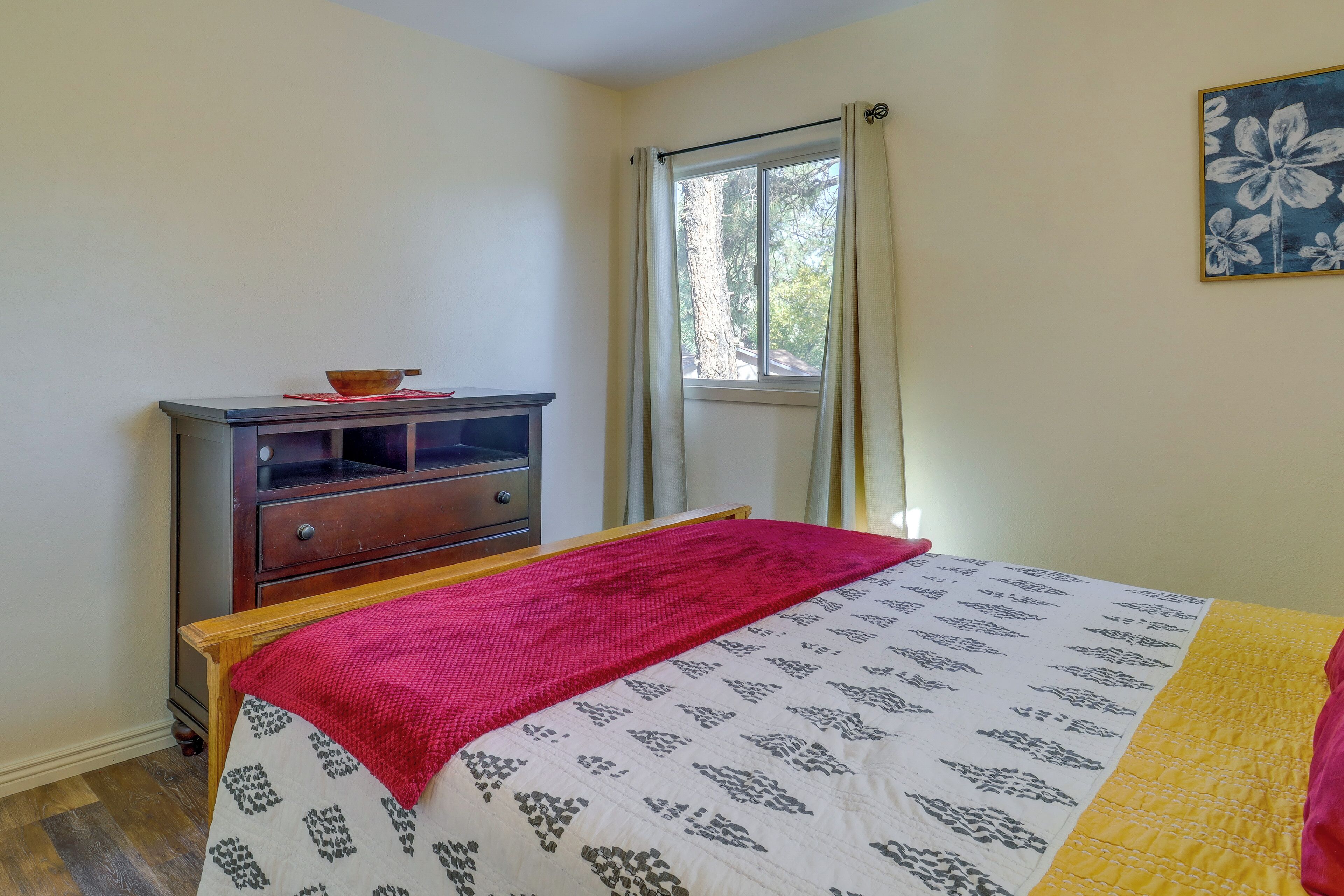 Een slaapkamer met een bed, een houten dressoir, een raam met gordijnen en een schilderij aan de muur.