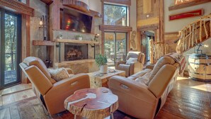 A spacious living area with leather sofas, a fireplace, and a large window overlooking a forest.