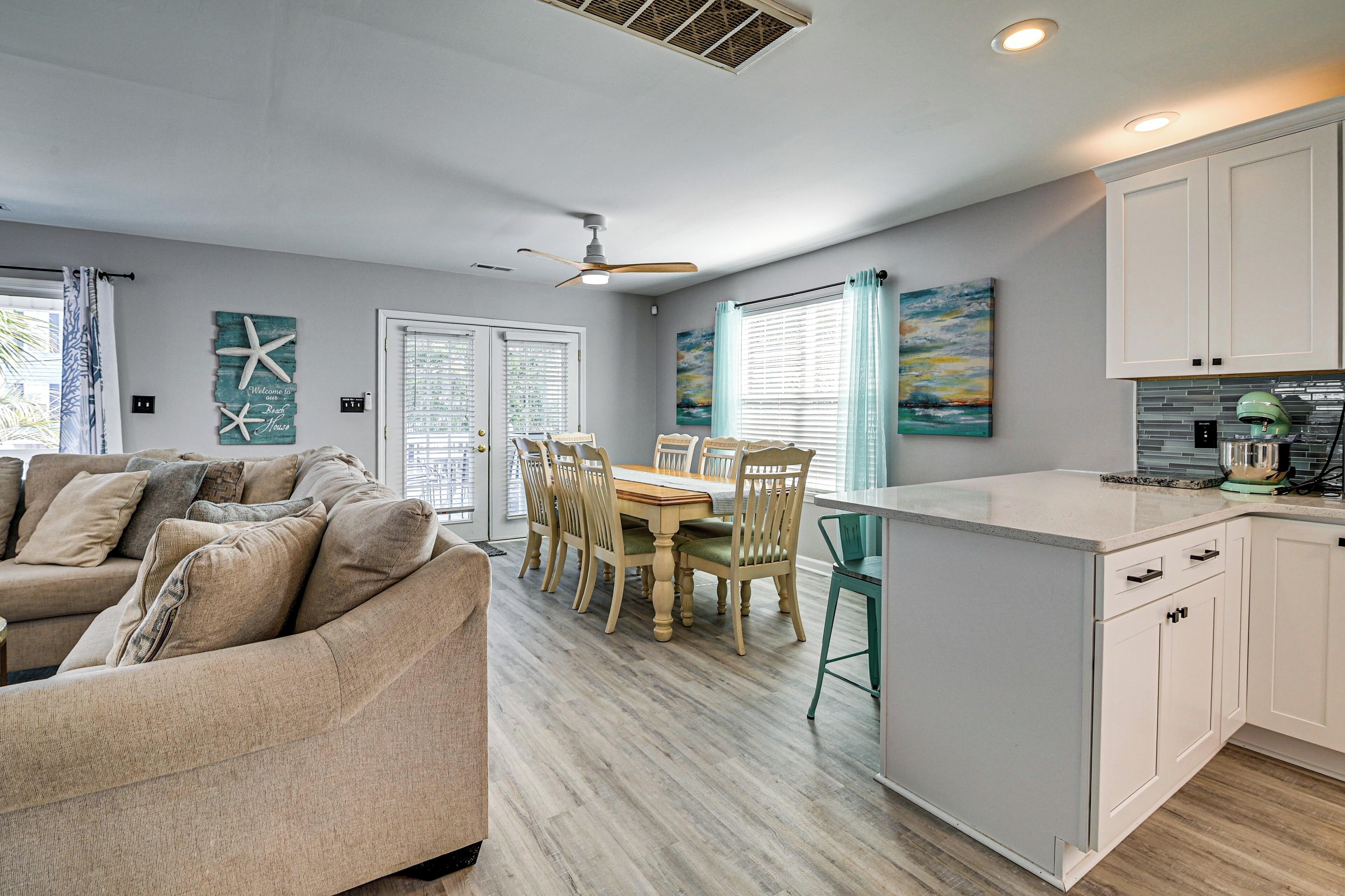 A modern kitchen with white cabinets, a dining area with a wooden table and chairs, and a ceiling fan.