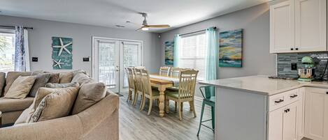 A modern kitchen with white cabinets, a dining area with a wooden table and chairs, and a ceiling fan.
