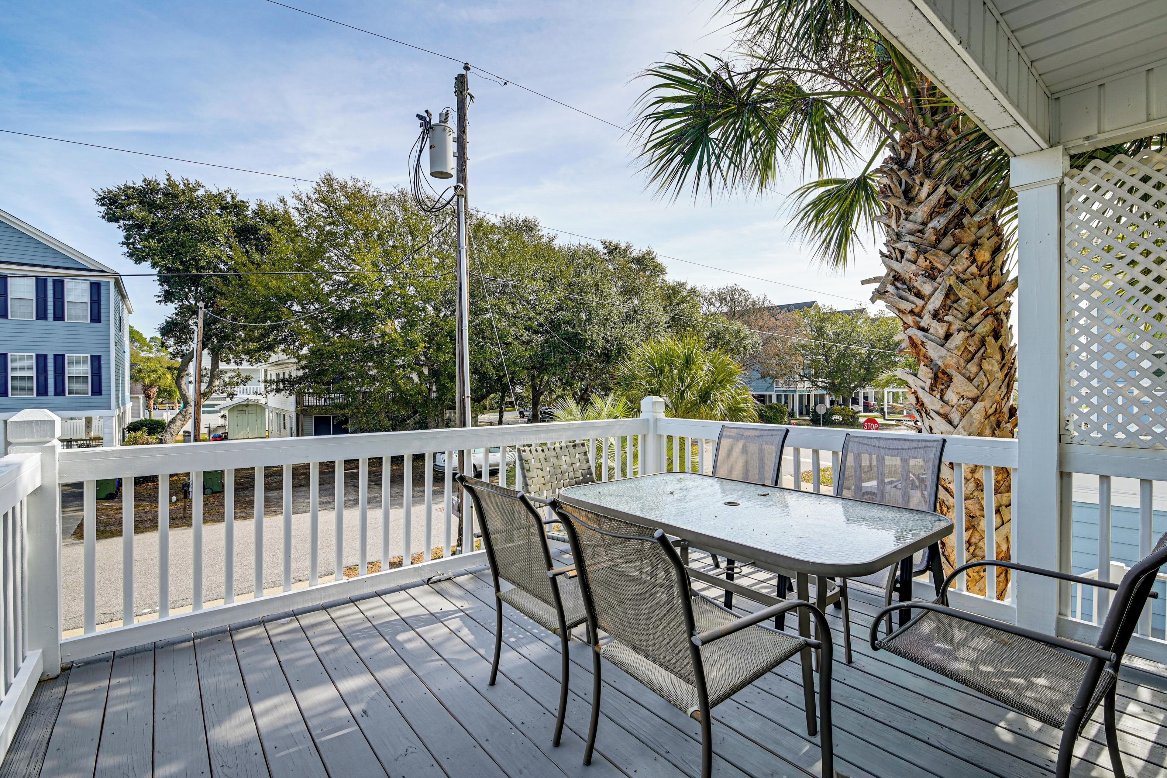 A covered outdoor deck with a table and chairs, surrounded by a white fence, overlooking a residential area.
