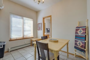 A dining area with a table, chairs, a window with blinds, a radiator, and a wall-mounted mirror.