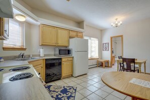 A kitchen with wooden cabinets, a microwave, a refrigerator, a stove, and a dining area with a table and chairs. - Charming Amalia Retreat w/ Fireplace & Grill! (Amalia)